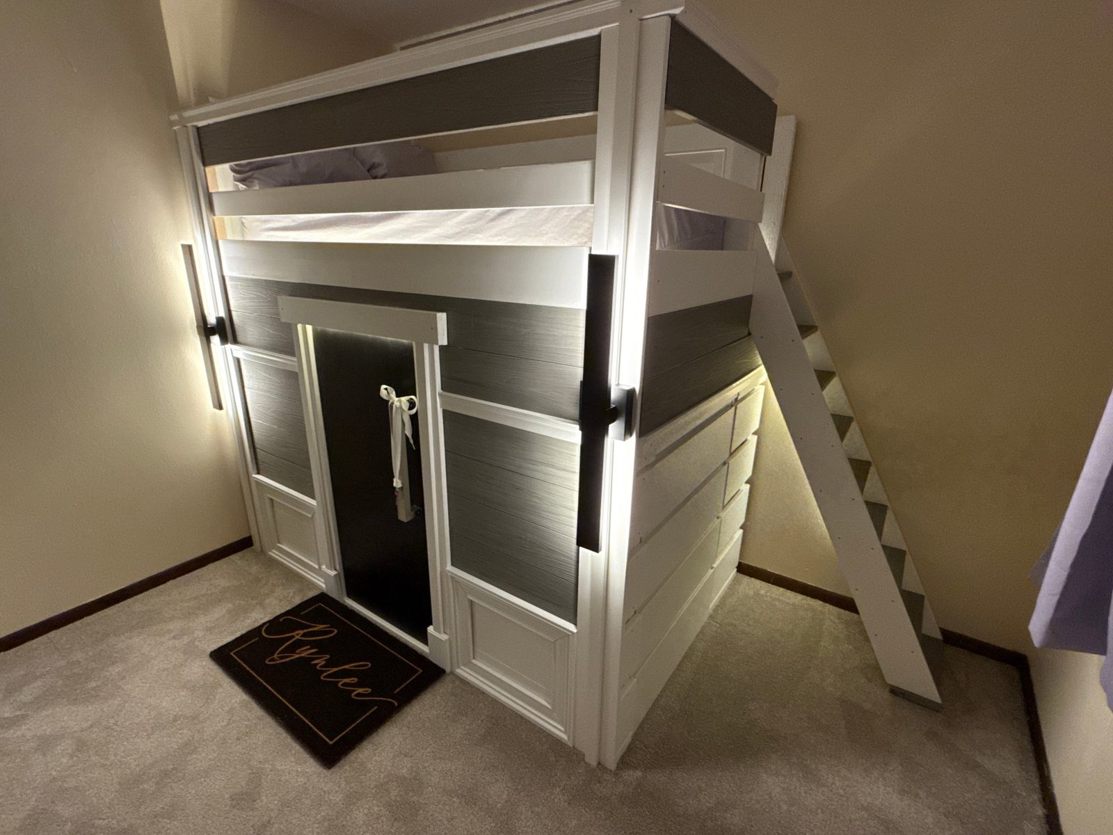 Three-quarter view of the finished playhouse — lit entry, staircase, storage fitted beneath the loft
