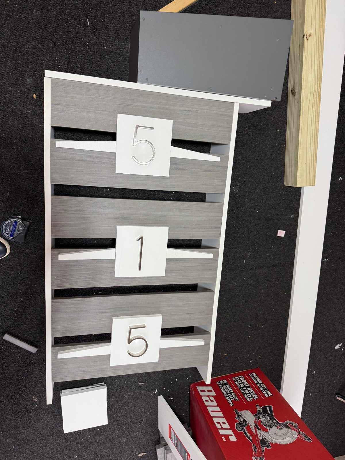 Mailbox post under construction on a workbench — horizontal composite slats with address numerals, enclosure set above